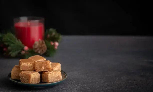Butterscotch Fudge on Plate with Christmas Candle on Dark Background with Copy Space Horizontal