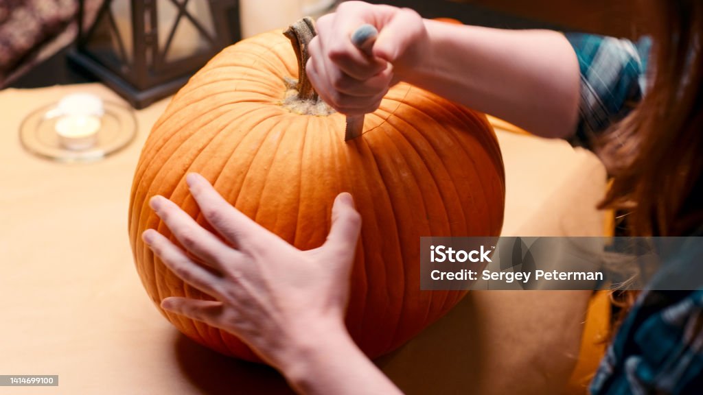 Woman carving Jack O Lantern pumpkin for Halloween Preparing pumpkin for Halloween. Woman sitting and carving with knife halloween Jack O Lantern pumpkin at home for her family. 30-34 Years Stock Photo