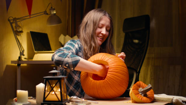 Woman carving Jack O Lantern pumpkin for Halloween Preparing pumpkin for Halloween. Woman sitting and pulling out face details of carved halloween Jack O Lantern pumpkin at home for her family. tug o stock pictures, royalty-free photos & images