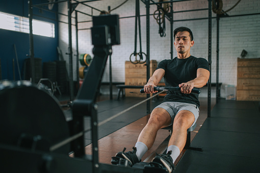 Asian Chinese Gay man exercising on rowing machine in a gym