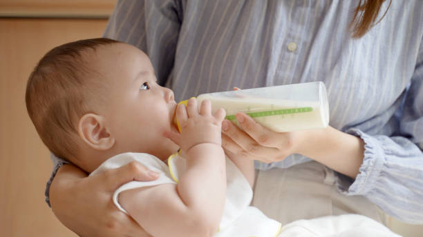 若いアジアの母親が赤ちゃんにミルクを与える - feeding bottle ストックフォトと画像
