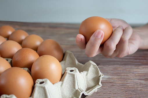 Woman's hand is pick up egg from paper packaging tray and holding it to preparing foods.