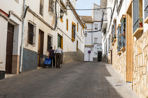 An elderly couple walking home, up a steep and quiet street, in the village of Olvera, Spain,