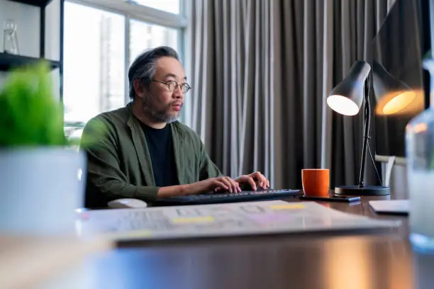 Mid adult man working at home on holiday,Home Office: a Happy Young Asian freelance creative man Working in the Comfort of His Home, Social Distancing Concept