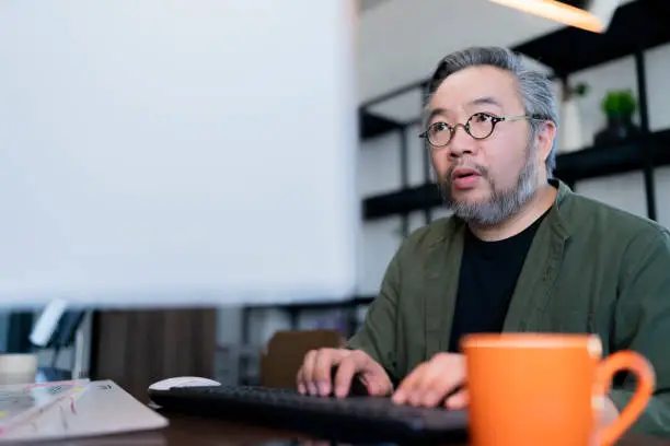 Mid adult man working at home on holiday,Home Office: a Happy Young Asian freelance creative man Working in the Comfort of His Home, Social Distancing Concept