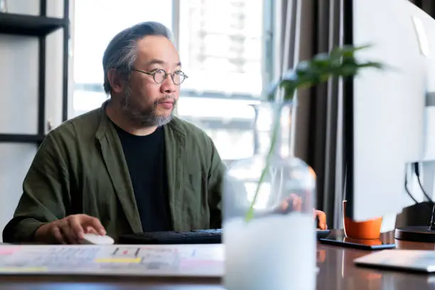 Mid adult man working at home on holiday,Home Office: a Happy Young Asian freelance creative man Working in the Comfort of His Home, Social Distancing Concept