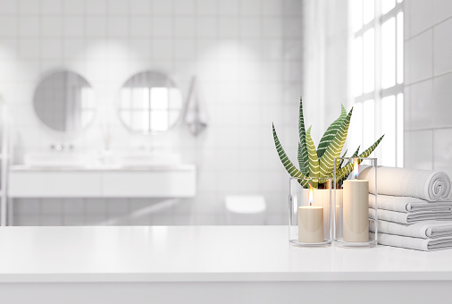 Blank white table top for copy space 3d render decorated with glass candle holders with flames. cotton towel and a potted plant with a blurry bathroom background.