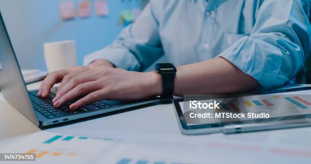 Closeup Young Asian Businessman Using Laptop Computer Look At Screen Scrolling Checking Reporting Presentation And Compare Data On Tablet At Small Business Workplace Overtime At Night Stock Photo - Download Image Now