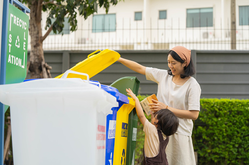 Asian mom teaching her son how to sort garbage before throwing it away.