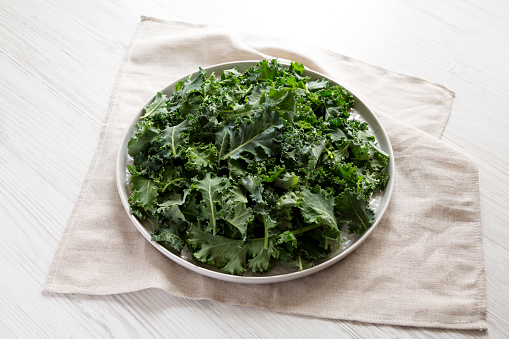 Raw Organic Baby Kale on a gray plate on a white wooden surface, side view.