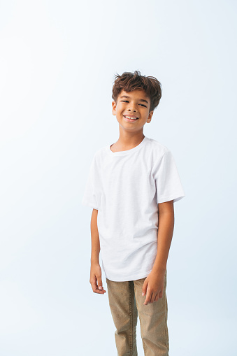 Half length portrait of a carefree Indian boy against bluish white background. He is wearing white T shirt. looking to the side.