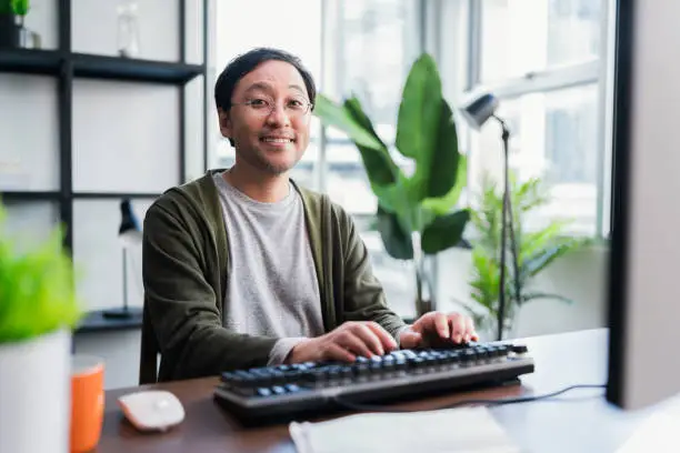 Asian adult man working at home on holiday,Home Office: a Happy Young Asian freelance creative man Working in the Comfort of His Home, Social Distancing Concept
