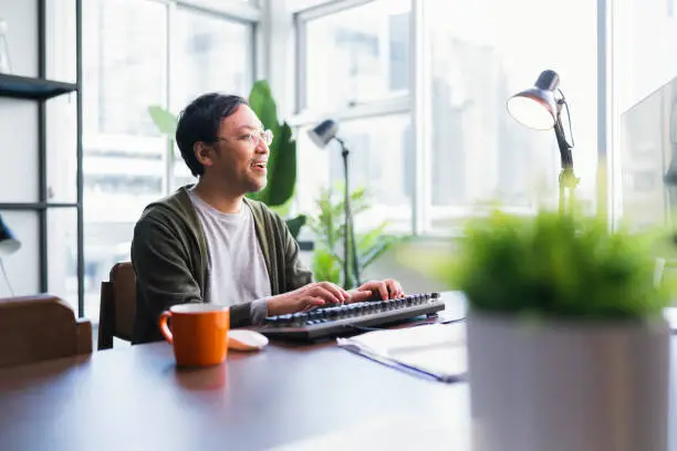 Asian adult man working at home on holiday,Home Office: a Happy Young Asian freelance creative man Working in the Comfort of His Home, Social Distancing Concept