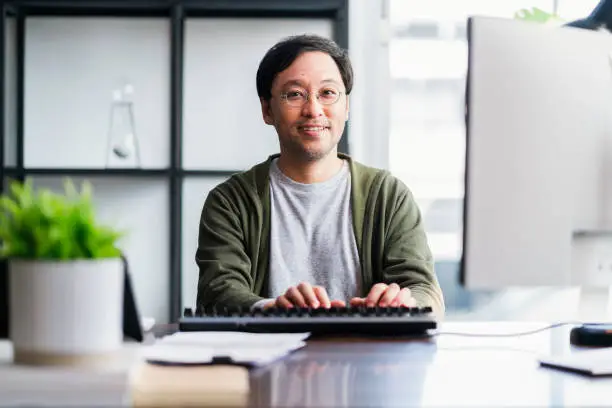 Asian adult man working at home on holiday,Home Office: a Happy Young Asian freelance creative man Working in the Comfort of His Home, Social Distancing Concept