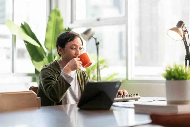 Asian adult man working at home on holiday,Home Office: a Happy Young Asian freelance creative man Working in the Comfort of His Home, Social Distancing Concept