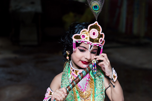 Little girl dressed up as Lord Krishna and smiling with flute. Janmashtami concept. Happy Krishna Janmashtami. Copy space.