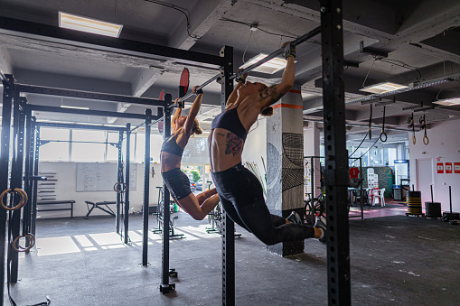 A side view of two determined female athletes exercising chin-ups during cross-training at the gym.