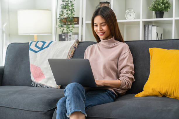 istock Cheerful young woman sitting on sofa and using laptop computer at home. 1414757203
