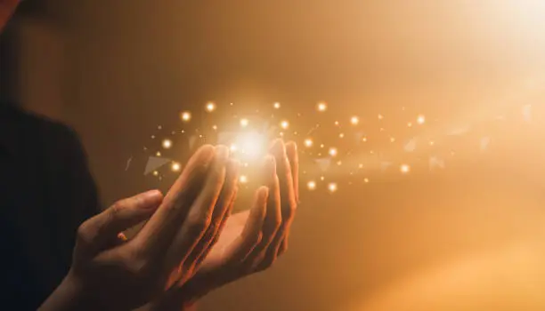 Hand praying with magic light that flows through on orange bokeh background.