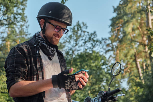 istock Young male biker in helmet using mobile phone and smiling sitting on a motorcycle 1414757723