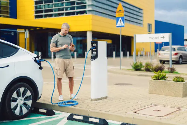 Man charging car at electric vehicle charging station before shopping