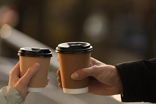 Couple with takeaway coffee cups outdoors, closeup
