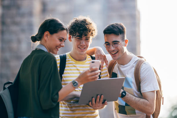 istock Happy Students Using Mobile Phone And Laptop Computer Together While Standing Outdoors 1414762877