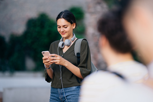 Cheerful smiling female student typing text message on her smartphone before class on campus.