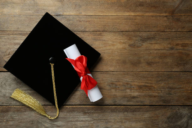 Graduation hat and diploma on wooden table, flat lay. Space for text