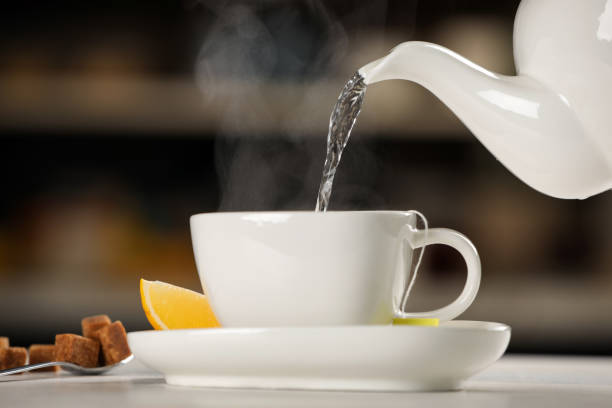 istock Pouring hot water into cup with tea bag at white table against blurred background 1414764823