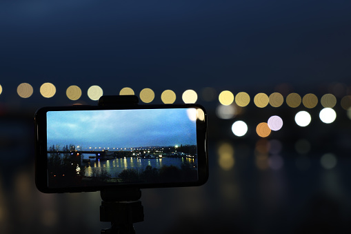 Taking photo with smartphone on tripod near river at night