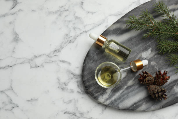 istock Pine essential oil, cones and branch on white marble table, top view. Space for text 1414764885