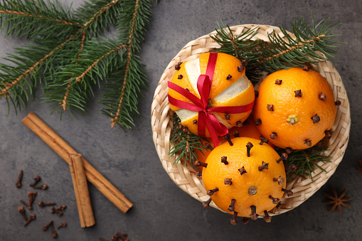 Pomander balls made of tangerines with cloves, spices and fir branches on grey table, flat lay