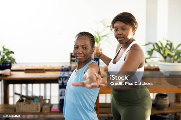 Female Yoga Instructor Adjusting Student Arm Position For Warrior 2 In Class Stock Photo - Download Image Now