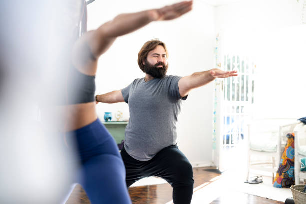 Gay man with beard in warrior pose in yoga class Gay man with beard in warrior pose in yoga class warrior 2 stock pictures, royalty-free photos & images