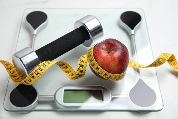 istock Scales, apple, measuring tape and dumbbell on white table 1414766479