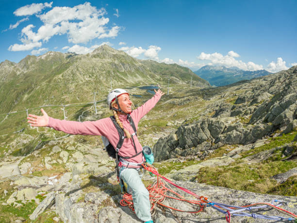 woman mountain climbing arms outstretched on mountain top - conquering adversity wilderness area aspirations achievement imagens e fotografias de stock