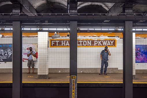 Fort Hamilton Parkway Station, Brooklyn, New York, NY, USA - July 6th 2022: Two persons standing on a subway platform seen across the tracks