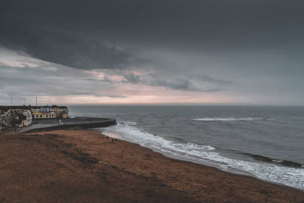 This is a horizontal, color photograph of the beach landscape in Fernandina Beach on Amelia Island in Florida on an overcast spring sunrise. Sea waves of the Atlantic shore crash on the coast. The horizon is over water in this seascape nature background.