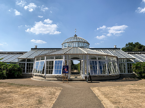 Fragment of facade of Grade1 listed greenhouse housing historic camelia plants at Chiswick House and Gardens in West London. Twilight, sunset, bench in bushes, green grass in front of the building. Glass house, orangerie