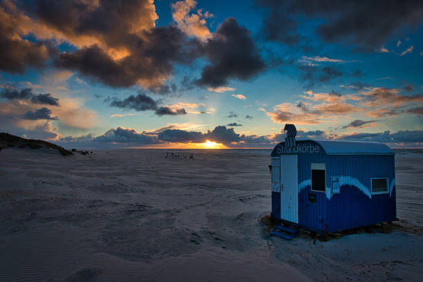 a beautiful sunset with luminous and dark clouds in the sky on a deserted beach on the island of Juist with a beach shack
