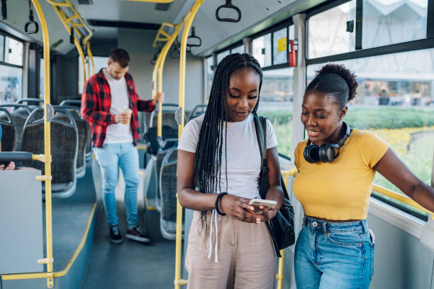 African american female friends talking while riding a bus in the city Two african american female passengers talking and using a smartphone while riding in a bus. Young black woman going to work by public transport. Young female friends browsing social network. riding stock pictures, royalty-free photos & images