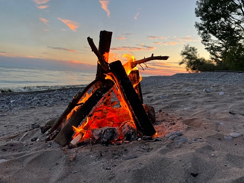 Burning logs on a rocky beach with a sunset sky