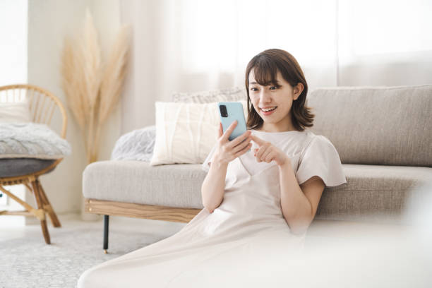 japanerin, die ein smartphone im zimmer bedient - hausfrau stock-fotos und bilder