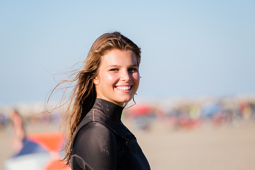 Portrait of kite surfing girl smiling in wetsuit with kitesurf on the beach. Water sports, and sporty woman concept