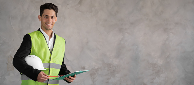 Young arabic architect with builder safety helmet over isolated background. happy builder face smiling while looking at camera. Positive person. banner, empty space