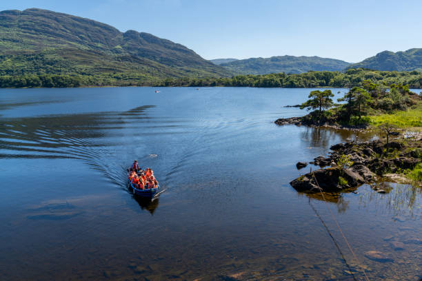 los turistas disfrutan de un paseo en bote por el lago muckross en el parque nacional killarney en un hermoso día de verano - lakes of killarney fotografías e imágenes de stock