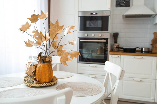 des branches avec des feuilles dorées et une citrouille sur un plateau. en arrière-plan, l’intérieur d’une cuisine blanche dans le style scandinave. le concept de confort de la maison. décor d’automne pour les vacances d’halloween. - autumn pumpkin flower food photos et images de collection