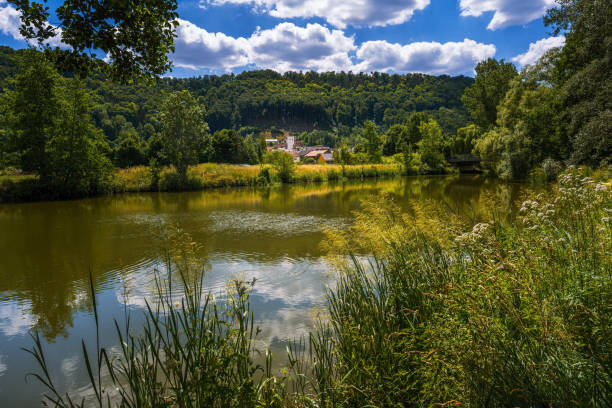 A serene view of a river surrounded by lush green hills under a bright blue sky with fluffy clouds