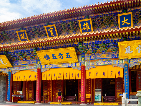 Xi'an, China - July 23, 2022: A man standing in front of a sprawling, colorful, traditional Chinese building. The building has different entrances and each entrance has a sign in Chinese Characters